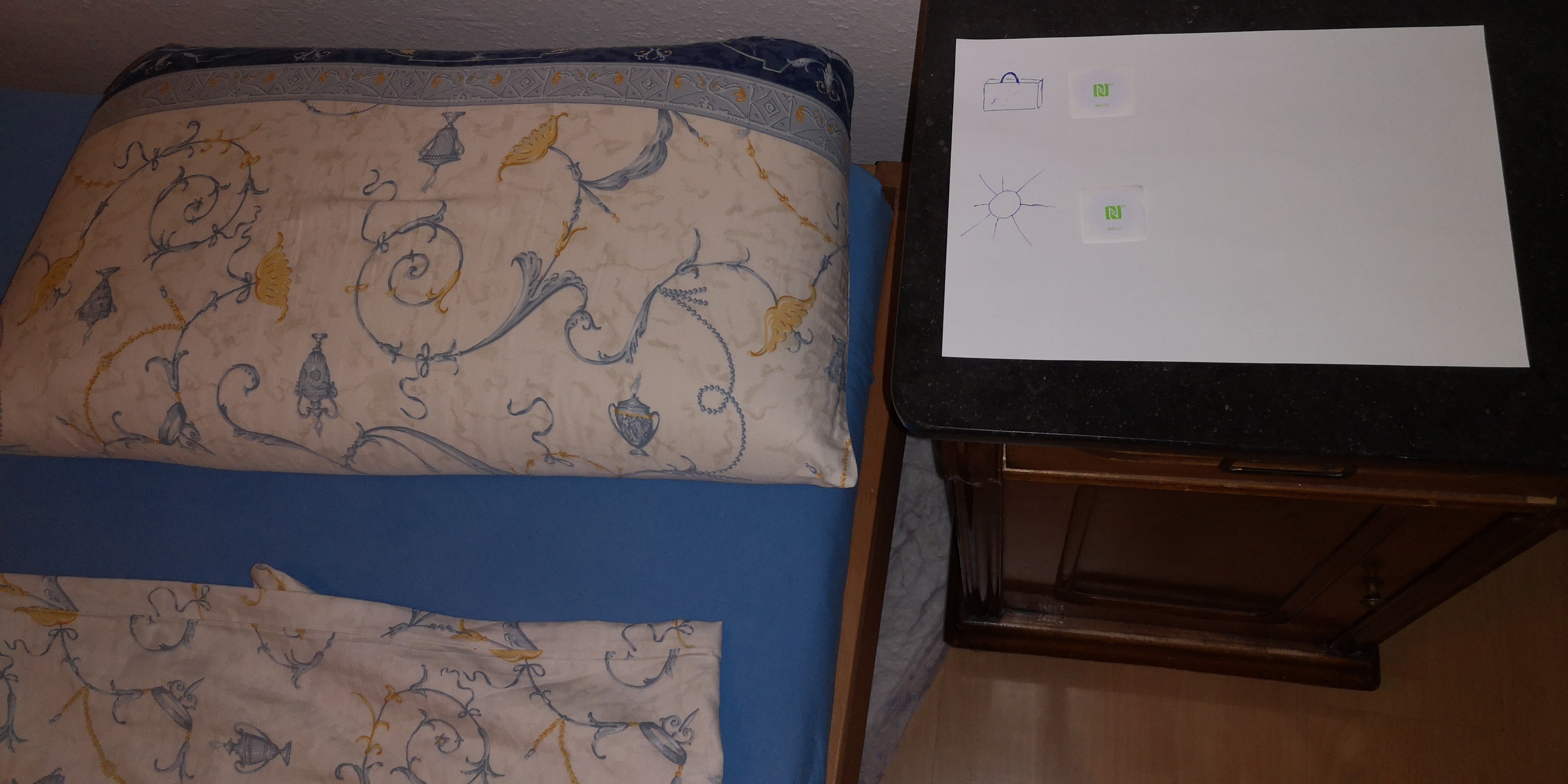 Bett und Nachttisch, auf dem Nachttisch sind zwei Symbole mit je einem NFC-Chip